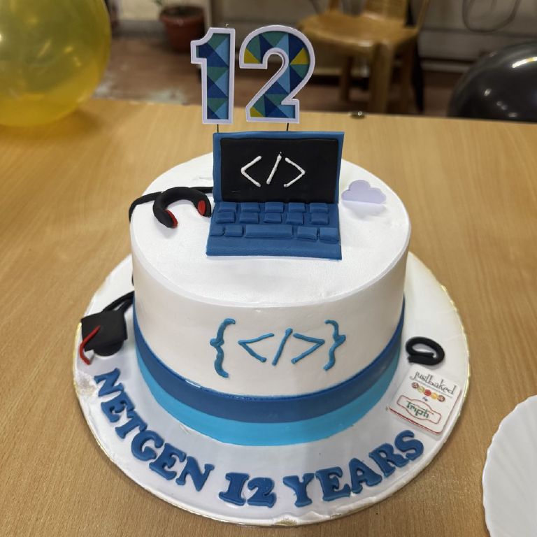 The twelfth-anniversary cake, topped with a fondant laptop showing a code symbol and a number 12, lettered Netgen 12 years