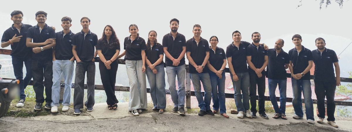 Fifteen members of the Netgen team in matching black shirts, standing in a row along a railing on a Shimla hillside