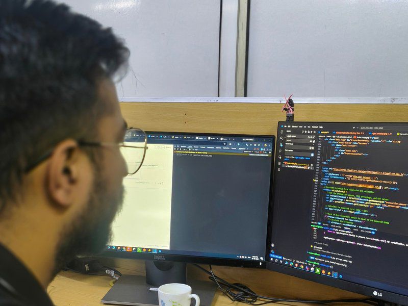 A Netgen developer reading code across two monitors at his desk in the Shimla office