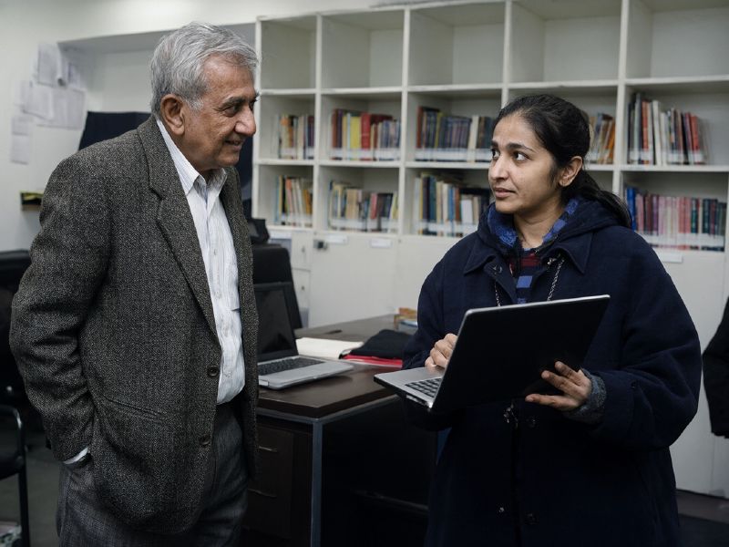Photo (AI-generated, illustrative): two college faculty members discuss a student progress dashboard on a laptop
