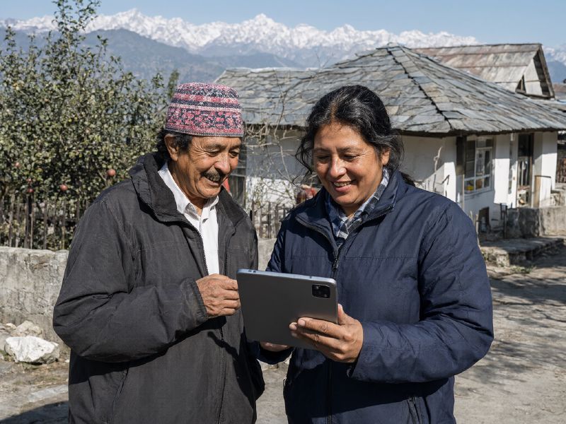 Photo (AI-generated, illustrative): a field officer enters data on a tablet while talking with a villager on a Himachal hillside