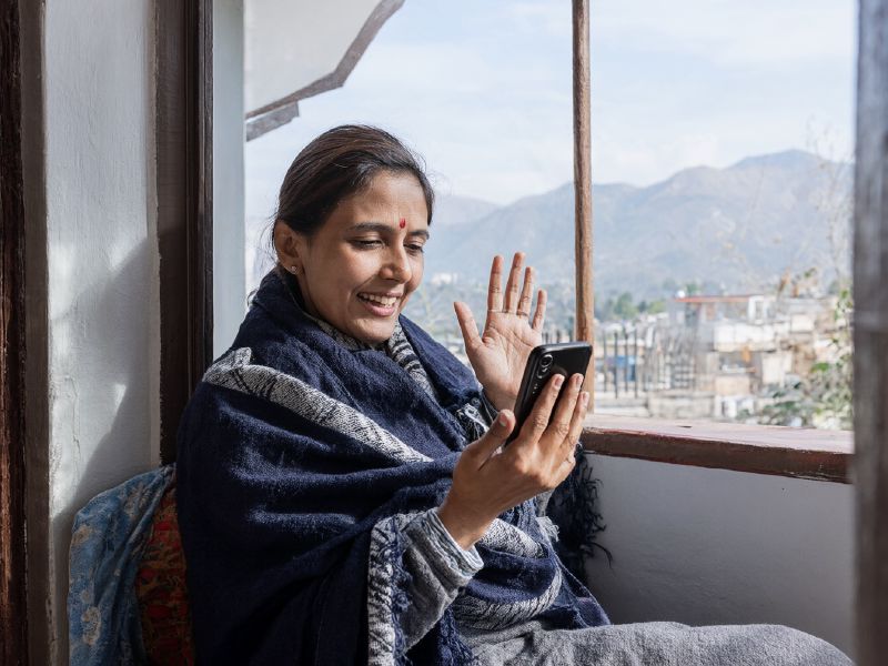 Photo (AI-generated, illustrative): a woman at home in a hill town on a video consultation with a doctor on her phone