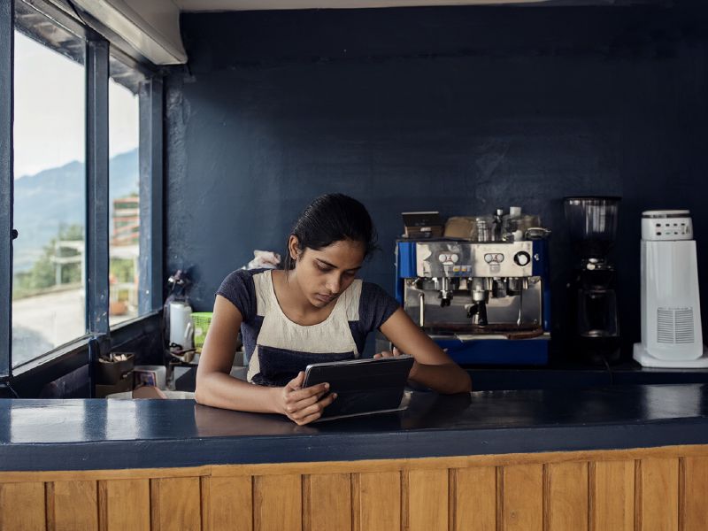 Photo (AI-generated, illustrative): a cafe owner reviews online orders and customer messages on a tablet at the counter