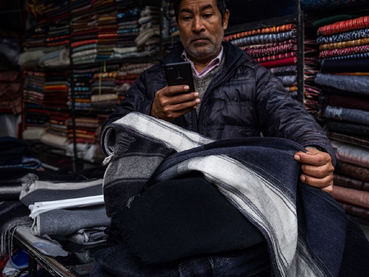 Photo (AI-generated, illustrative): a shawl shopkeeper photographs a shawl with his phone for his online store