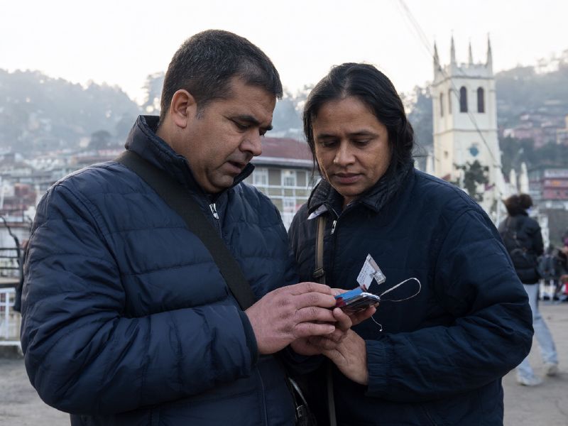 Photo (AI-generated, illustrative): a tourist couple on Mall Road, Shimla, checking a hotel booking on a phone