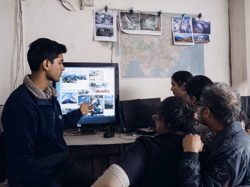 Photo (AI-generated, illustrative): a tour operator shows a family a trek package on a large monitor